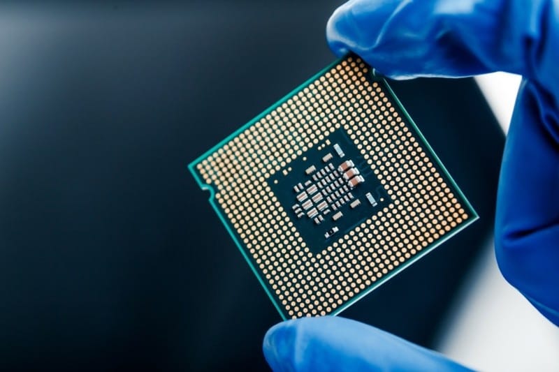 A computer CPU being held in blue-gloved hands, showcasing its intricate design and gold pins.