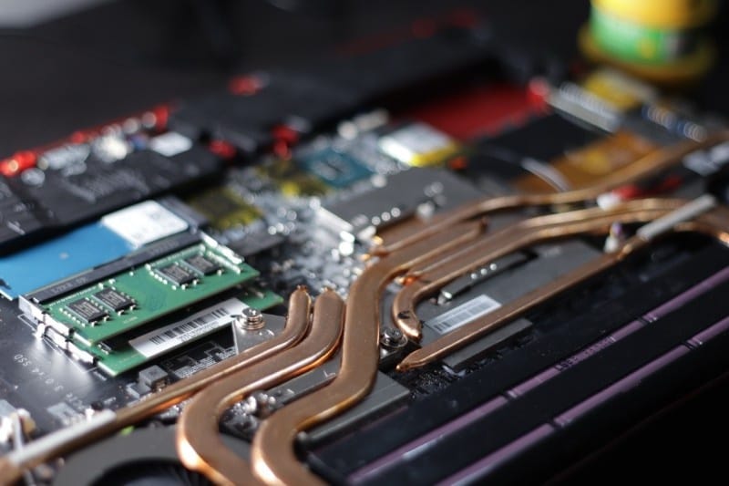 An assembly of computer parts showcasing RAM, a motherboard, and copper heat pipes for cooling in a laptop.