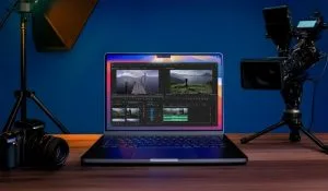 Filmmaker-Approved Tips for Picking the Ultimate Laptop. A laptop displaying video editing software alongside a video camera and a DSLR camera, set in a studio environment.