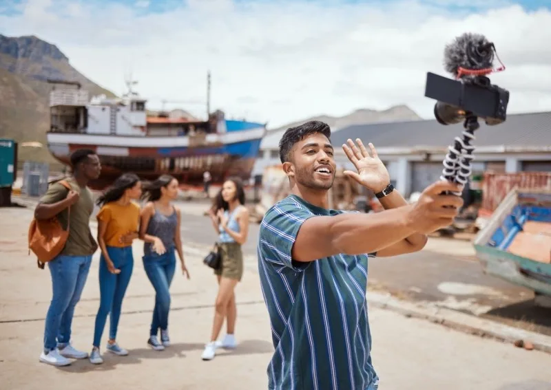 A young man vlogging with a smartphone while his friends interact in a vibrant outdoor setting.