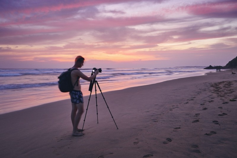 A photographer capturing a vibrant sunset on the beach with a tripod and camera.