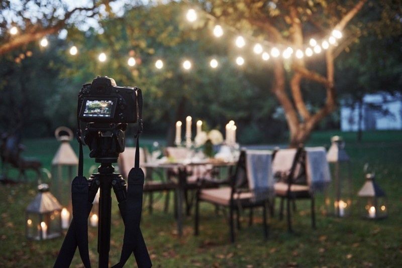 A well-set outdoor dining table with ambient lighting, showcasing a DSLR camera on a tripod in the foreground.