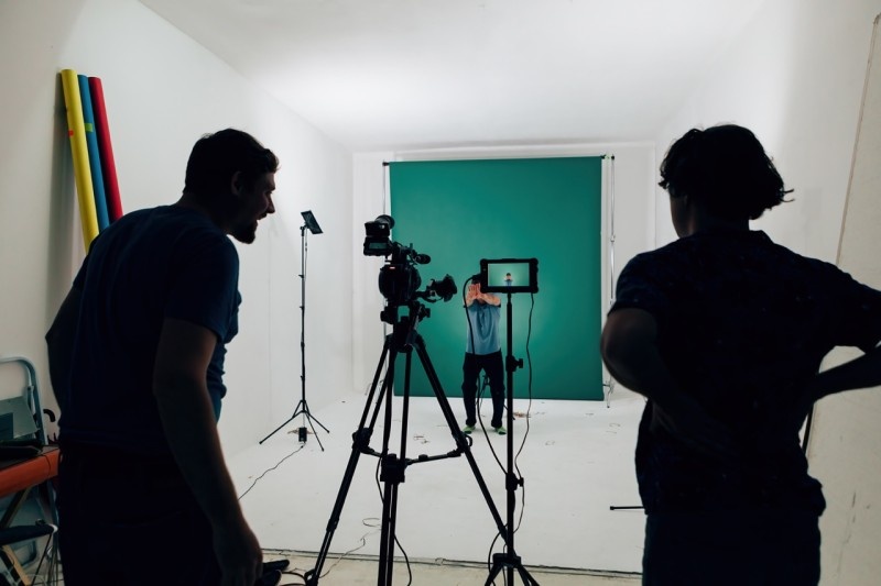 A photography studio set up with cameras and lighting, featuring a model in front of a green backdrop.