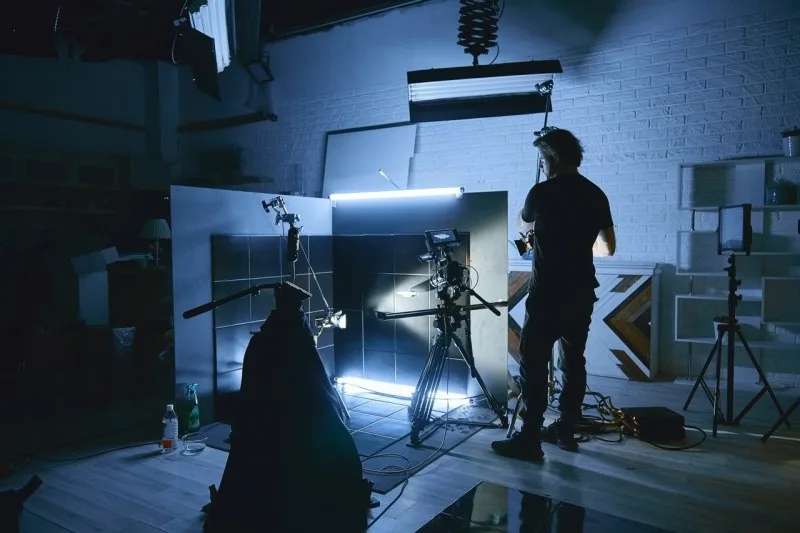 A photography studio setup with lighting equipment, camera on tripod, and a silhouetted figure preparing for a shoot.