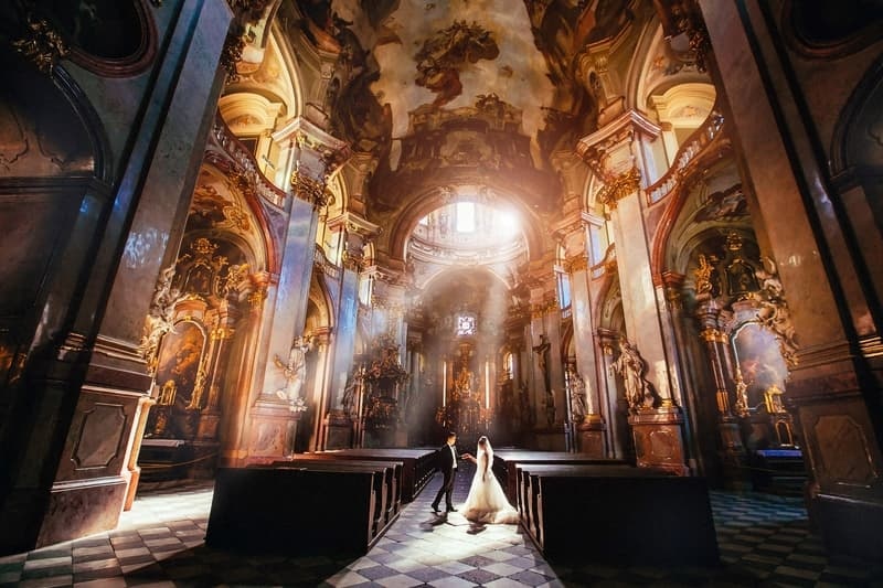 A bride and groom standing in a beautifully illuminated church, showcasing stunning architecture and decor.