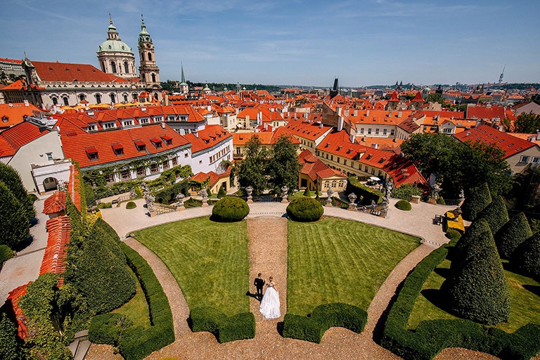 A breathtaking aerial view of a wedding couple in a scenic garden overlooking the historic city with red roofs and churches in the background.