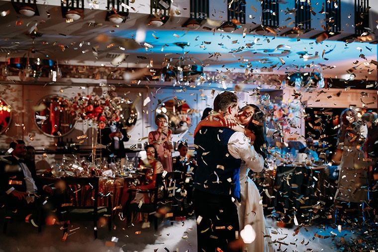 Couple dancing at a wedding reception surrounded by confetti and guests celebrating.