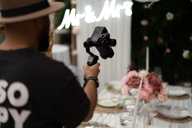 A videographer capturing the wedding setup featuring the 'Mr & Mrs' sign, elegant table settings, and floral decor.