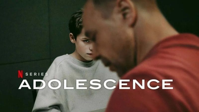 A tense scene from the Netflix series 'Adolescence' featuring a young boy with a serious expression sitting across from an adult man.