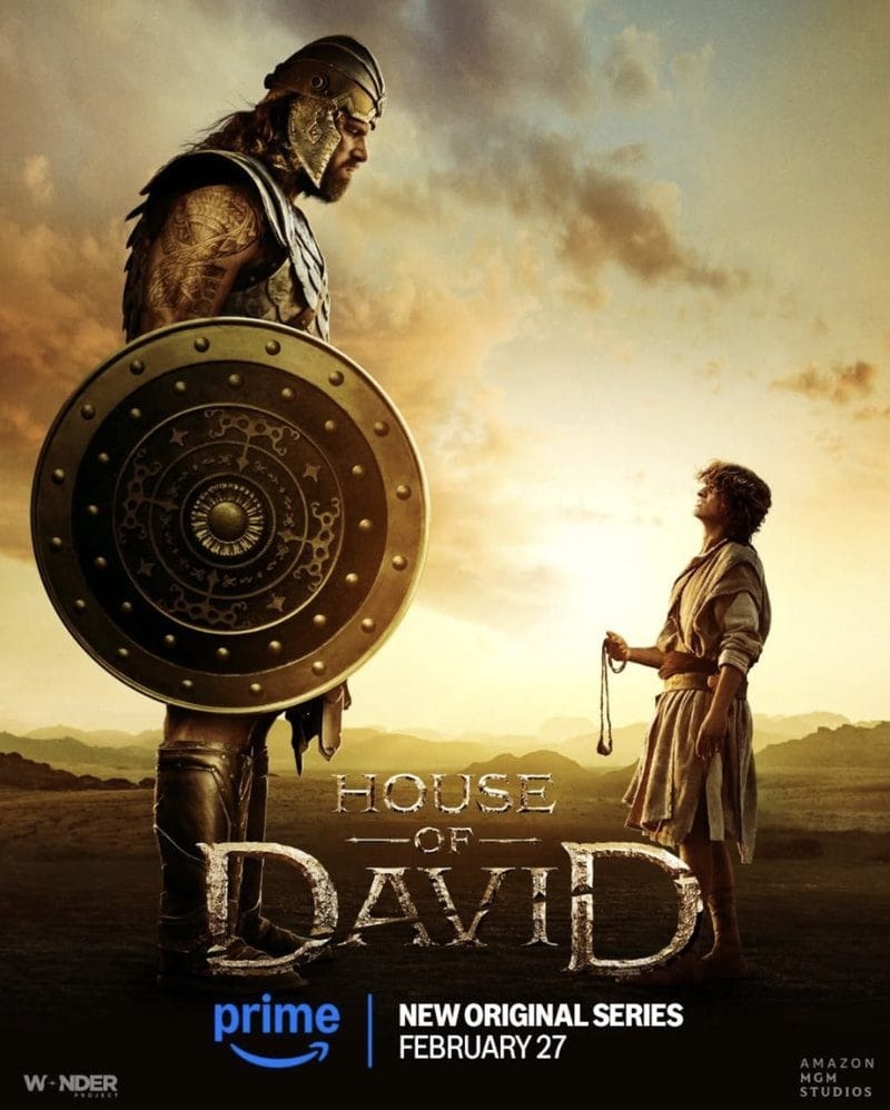 A scene from the upcoming series 'House of David', showcasing a giant warrior in armor alongside a young figure, set against a dramatic sunset, embodying themes of strength and bravery.